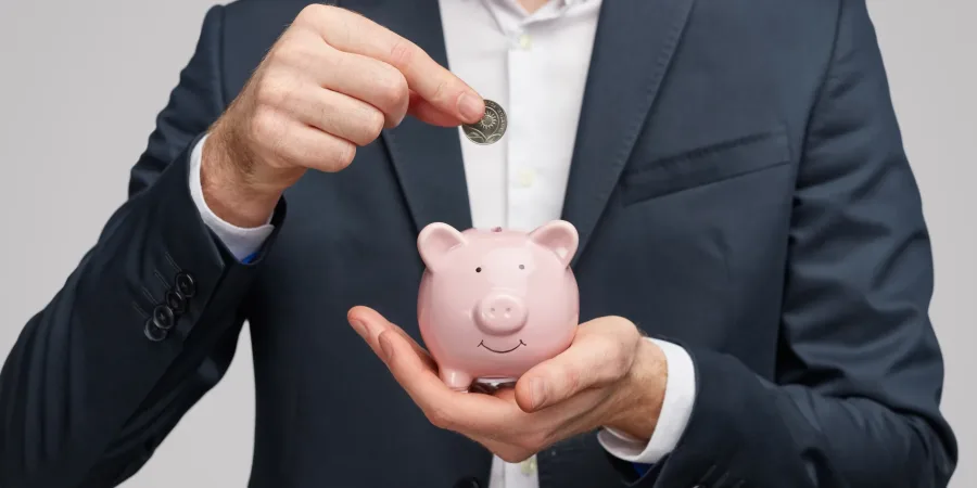 Crop businessman inserting coin in piggy bank